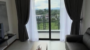 A living room with a TV, a sofa, and a balcony with curtains. - Apartments @ Podium Kuching (Kuching)