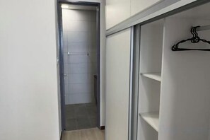 A narrow hallway with a door leading to a tiled room, a closet with shelves, and a coat rack. - Apartments @ Podium Kuching (Kuching)