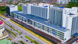 A modern building with a glass facade, multiple floors, and a parking lot in front. - Apartments @ Podium Kuching (Kuching)