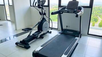 A gym with a treadmill, elliptical, and stationary bike, large windows with a view of greenery.