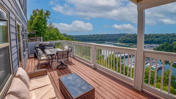 Una terraza techada con mobiliario exterior, vista a un lago y una colina boscosa al fondo.