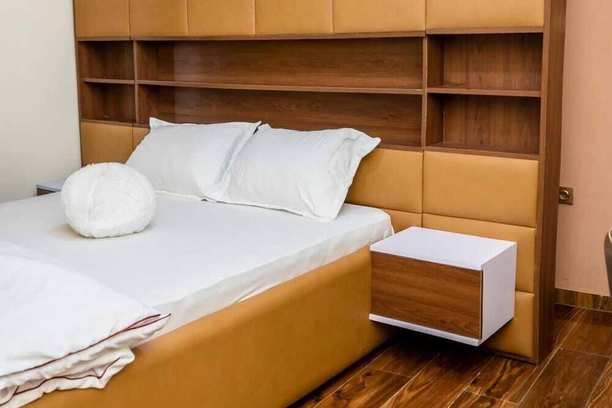 A bedroom with a large bed, a wooden headboard, a bedside table, and a wardrobe with multiple shelves.