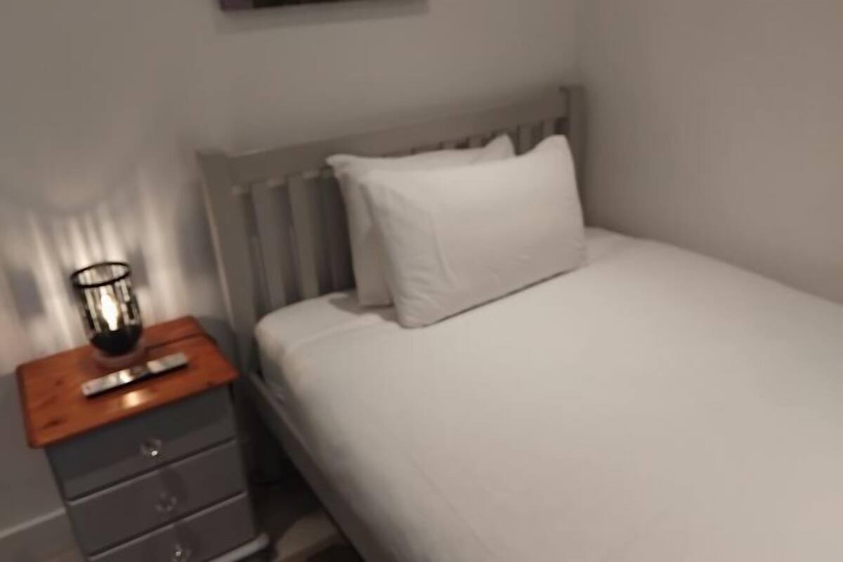 A single bed with white bedding, a wooden nightstand with a remote control, and a drawer.