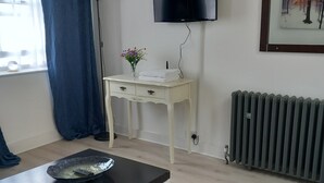 A living room with a flat-screen TV mounted on the wall, a white side table with a vase of flowers, a black coffee table, a patterned rug, and a radiator. - Number Four  (Brighton)