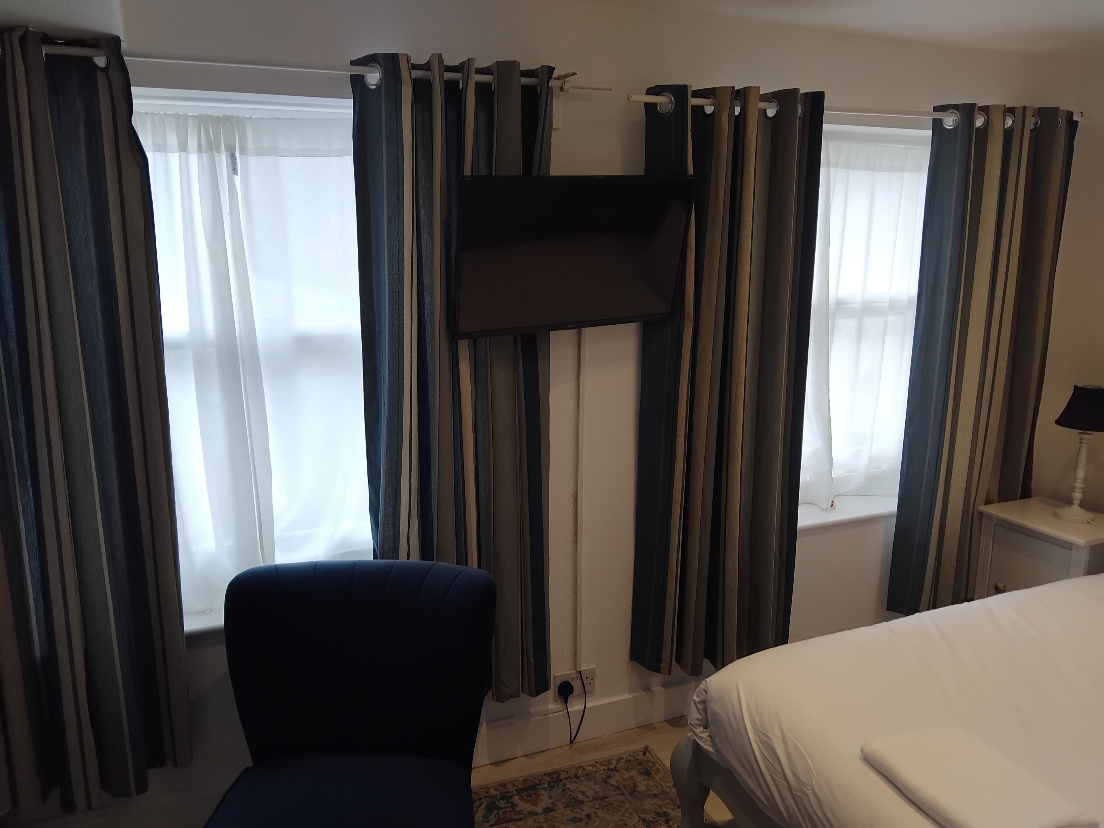 A hotel room with a bed, a chair, a TV mounted on the wall, and curtains on the windows.