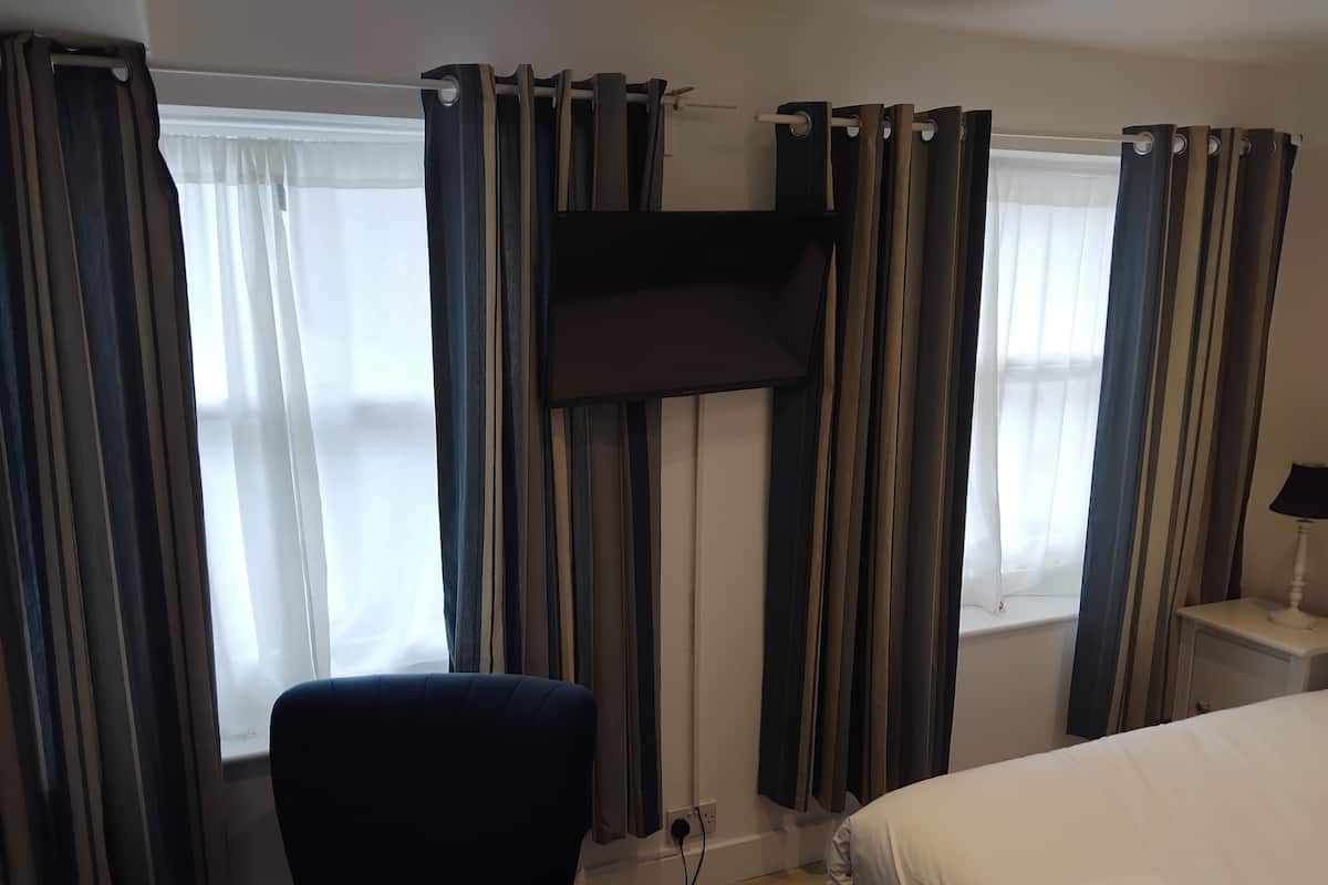 Ett hotellrum med en säng, en stol, en tv som är monterad på väggen och gardiner vid fönstren.