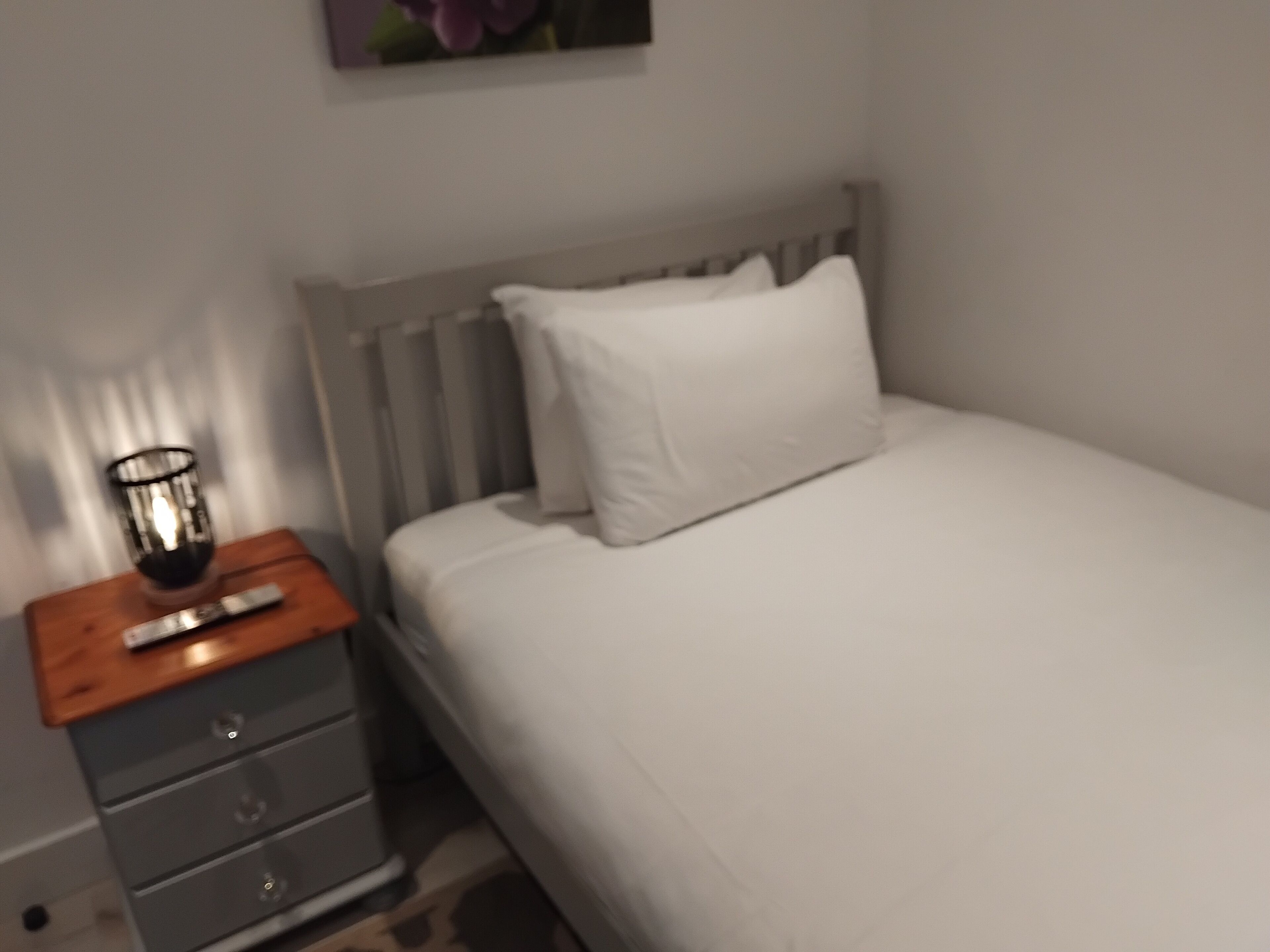 A bedroom with a bed, a nightstand, a lamp, and a dresser.