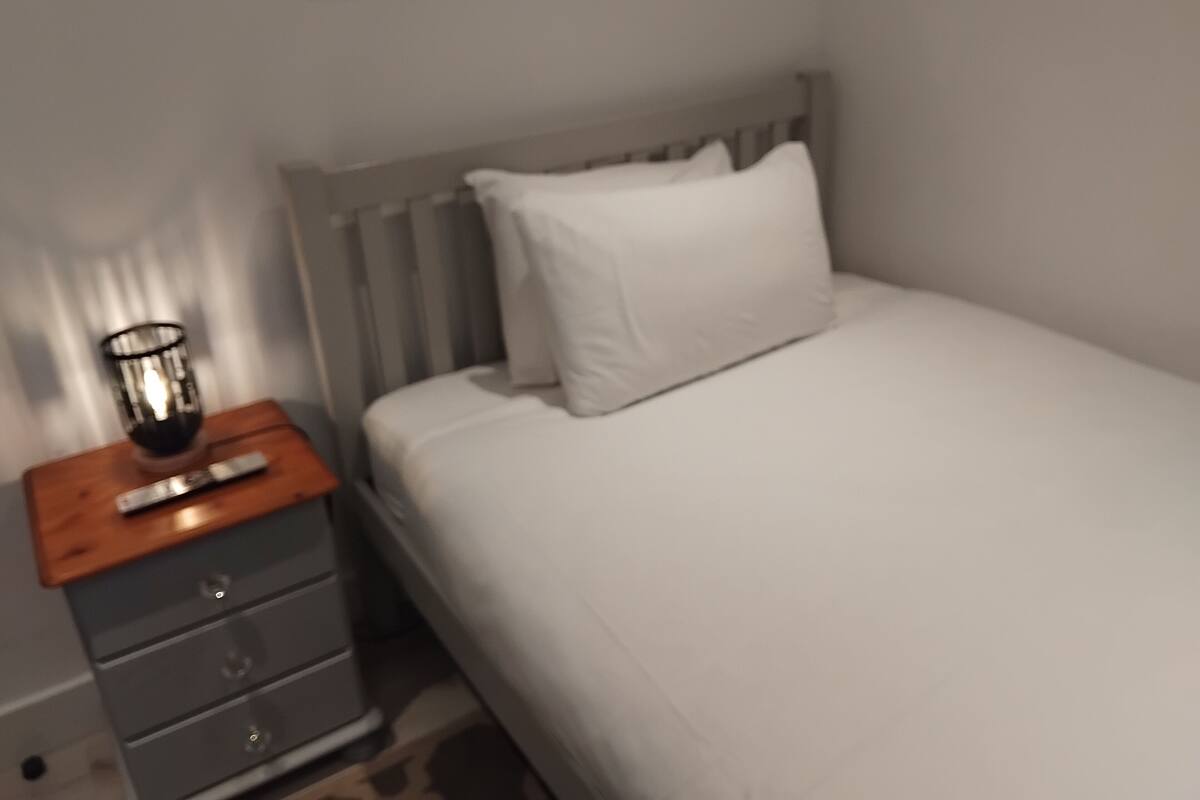 A bedroom with a bed, a nightstand, a lamp, and a dresser.