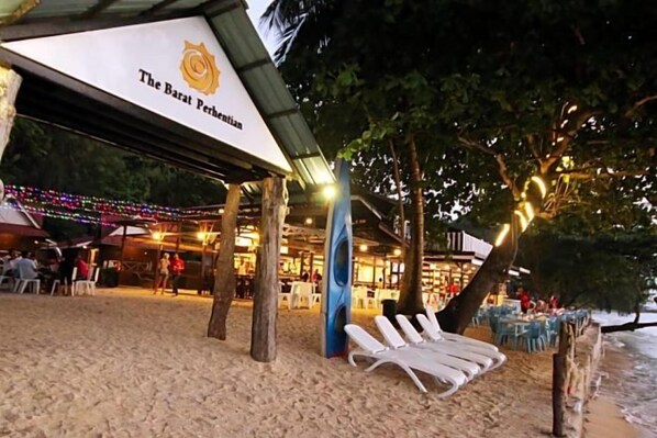 A beachside bar with a canopy, lounge chairs, and a sign for 'The Barat Perhentian'.