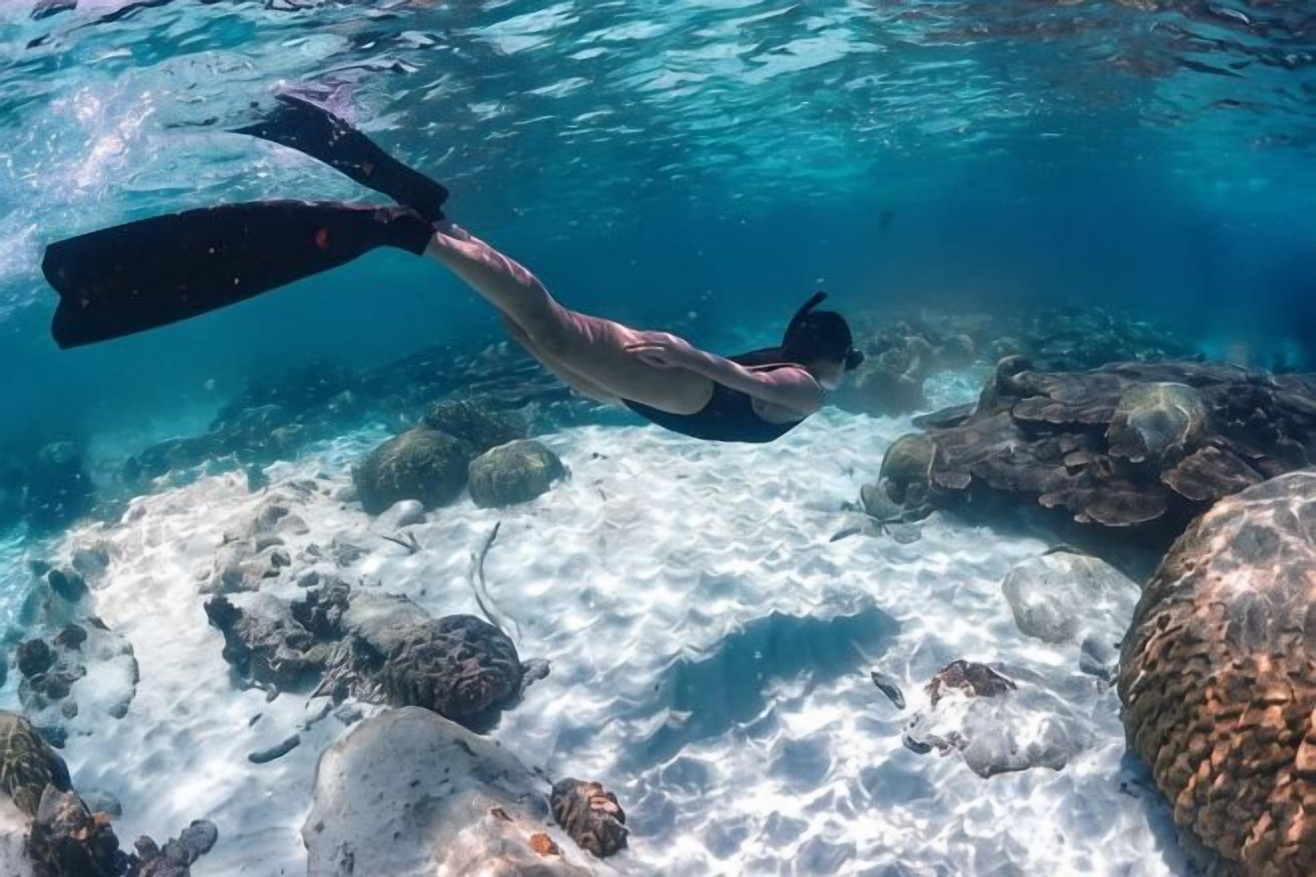A person snorkeling underwater with rocks and clear water.