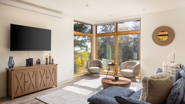 Una sala de estar moderna con un televisor grande, asientos cómodos y grandes ventanales con vistas a árboles.