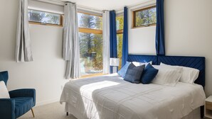 Un dormitorio con una cama grande, una mesita de noche, una silla y una ventana con cortinas.