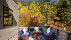 Una terraza con mobiliario de mimbre y una mesa de vidrio, con vistas a un bosque con follaje otoñal.