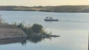 A view of a calm lake with a boat in the distance, surrounded by hills and a clear sky.