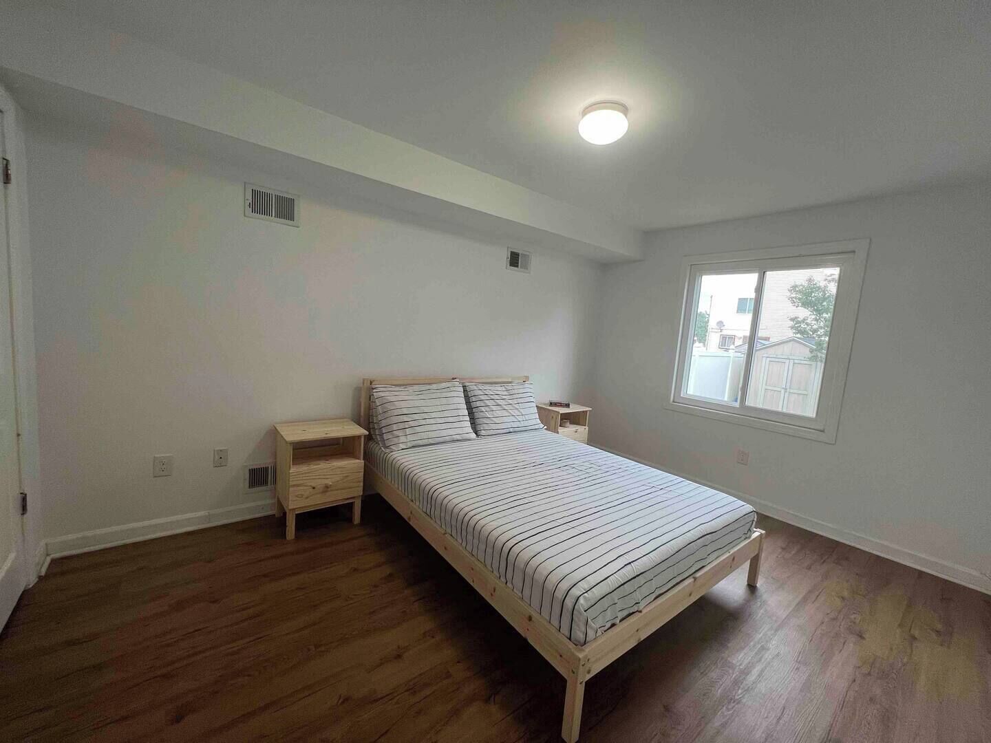 A bedroom with a wooden bed, a nightstand, a window, and a ceiling light.