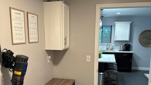 A laundry area with a washing machine, a vacuum cleaner, and a table. - Double Up In Delano-by Dtwn Stadium&ballpark Arena (Wichita)
