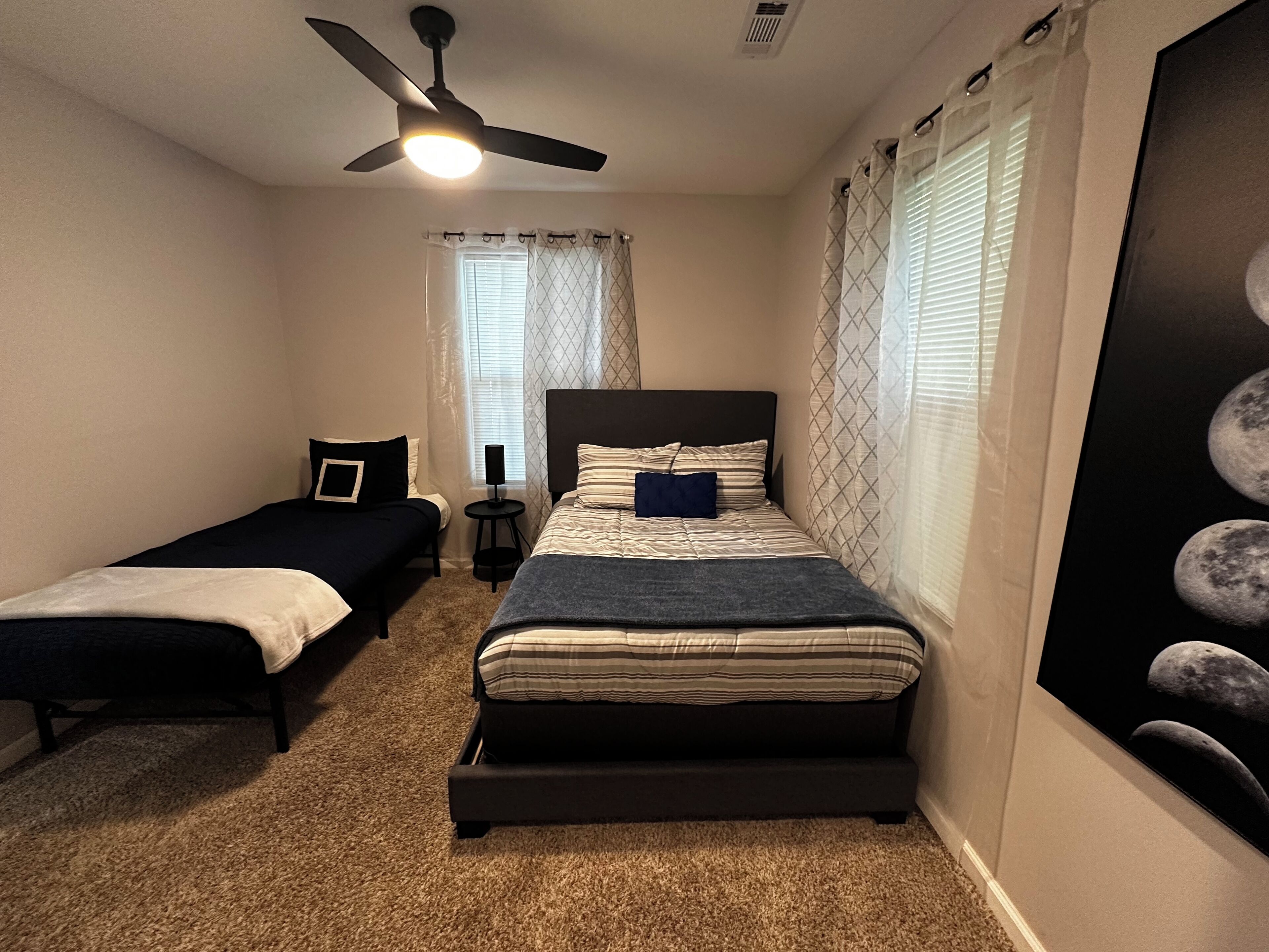 A bedroom with two single beds, a ceiling fan, a nightstand, a lamp, and a window with curtains.
