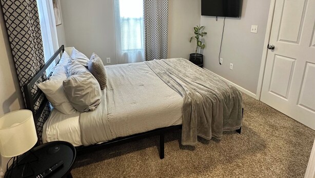 A bedroom with a bed, a ceiling fan, a TV, and a carpeted floor. - Double Up In Delano-by Dtwn Stadium&ballpark Arena (Wichita)
