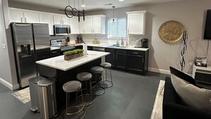 A modern kitchen with white cabinets, stainless steel appliances, and a central island with stools. - Double Up In Delano-by Dtwn Stadium&ballpark Arena (Wichita)
