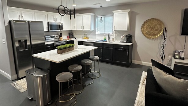 A modern kitchen with white cabinets, stainless steel appliances, and a central island with stools. - Double Up In Delano-by Dtwn Stadium&ballpark Arena (Wichita)