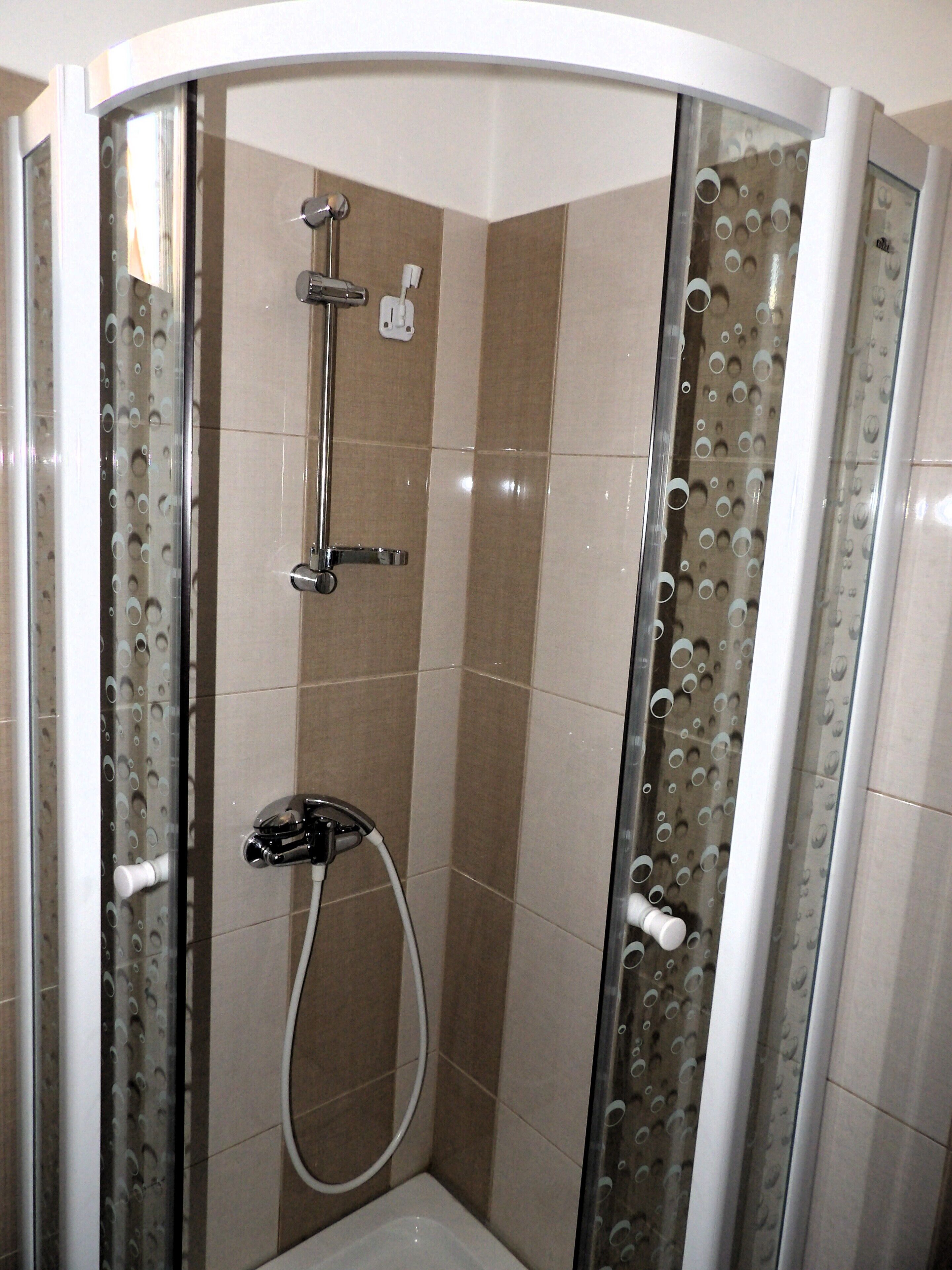 A glass-enclosed shower with a handheld showerhead and a wall-mounted faucet.