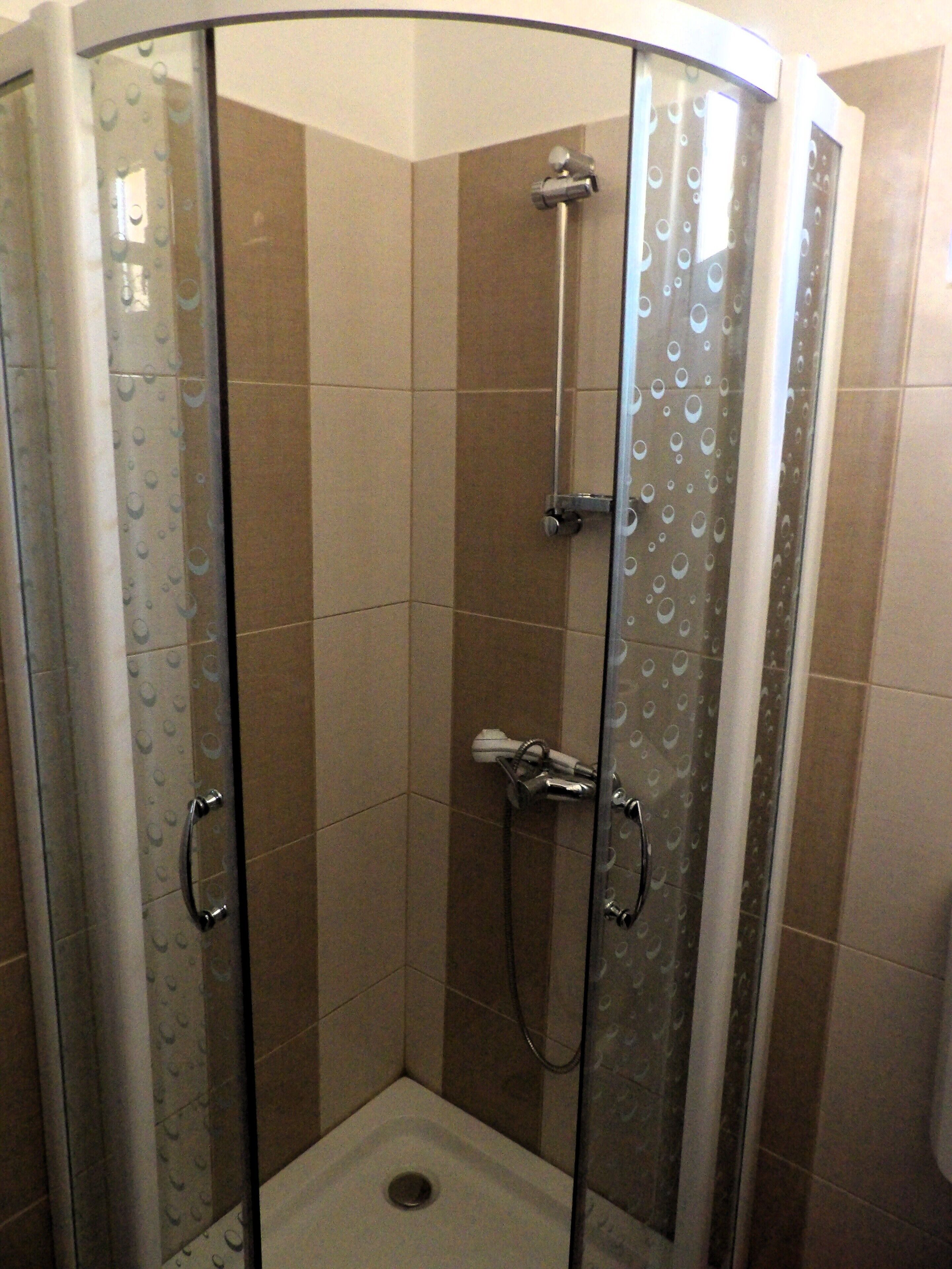 Une cabine de douche fermée par des parois en verre, équipée d’un pommeau de douche à main et d’un flexible de douche à main.