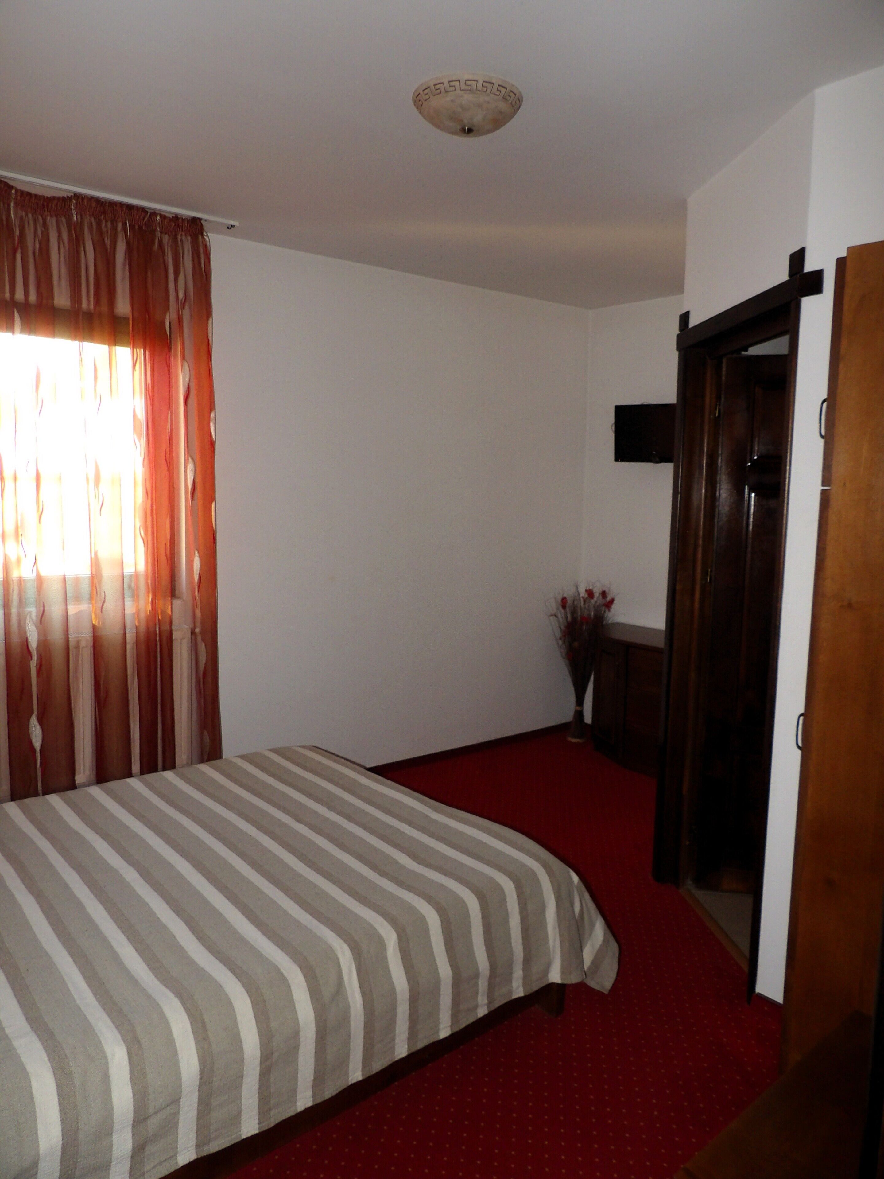Een slaapkamer met een bed, een houten garderobe, een kleine tafel met een vaas en een rood tapijt.