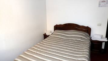 A single bed with a striped bedspread, a wooden headboard, a nightstand with a telephone, and a wall-mounted light switch.