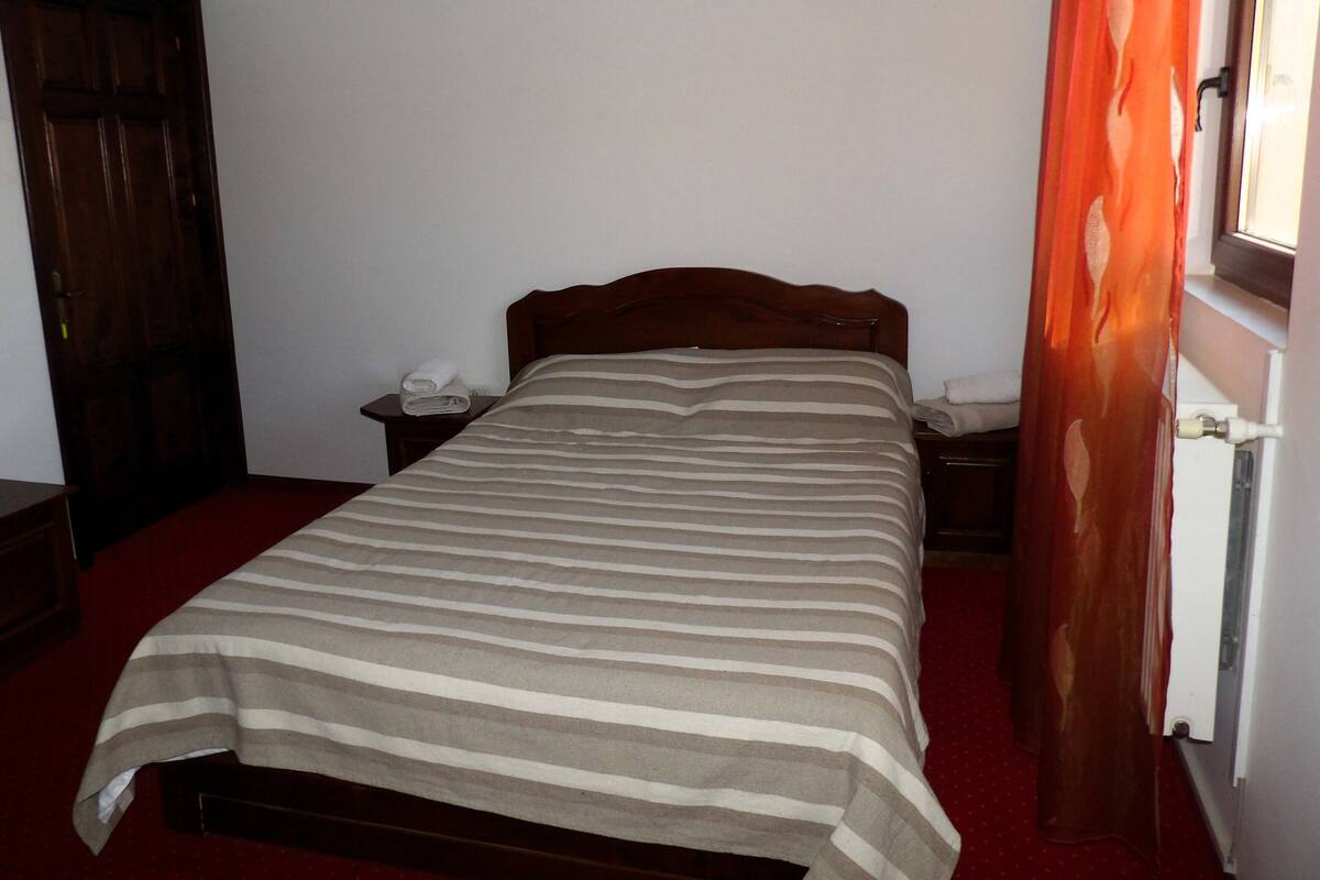 A single bed with a striped bedspread, a wooden headboard, a nightstand with a telephone, and a red carpeted floor.