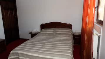 A single bed with a striped bedspread, a wooden headboard, a nightstand with a telephone, and a red carpeted floor.
