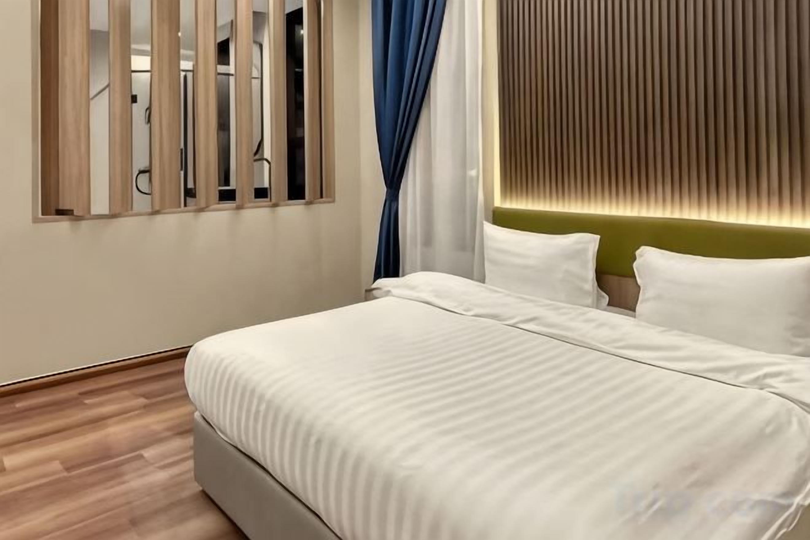 Habitación de hotel moderna con una cama grande, cabecera de madera y vistas a través de una ventana con persianas verticales.