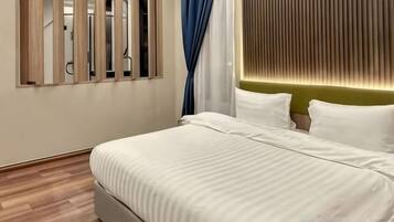 Habitación de hotel moderna con una cama grande, cabecera de madera y vistas a través de una ventana con persianas verticales.