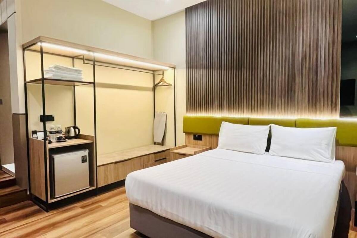 A modern hotel room with a large bed, a built-in wardrobe, a small kitchenette, and a wall-mounted TV.
