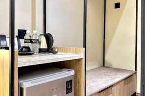 A compact hotel room with a kitchenette, a small seating area, and a wall-mounted TV.