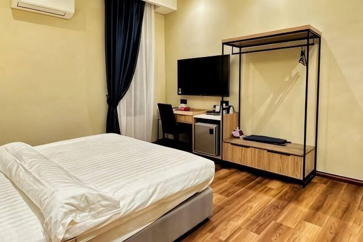 A hotel room with a bed, desk, chair, TV, and a wardrobe.