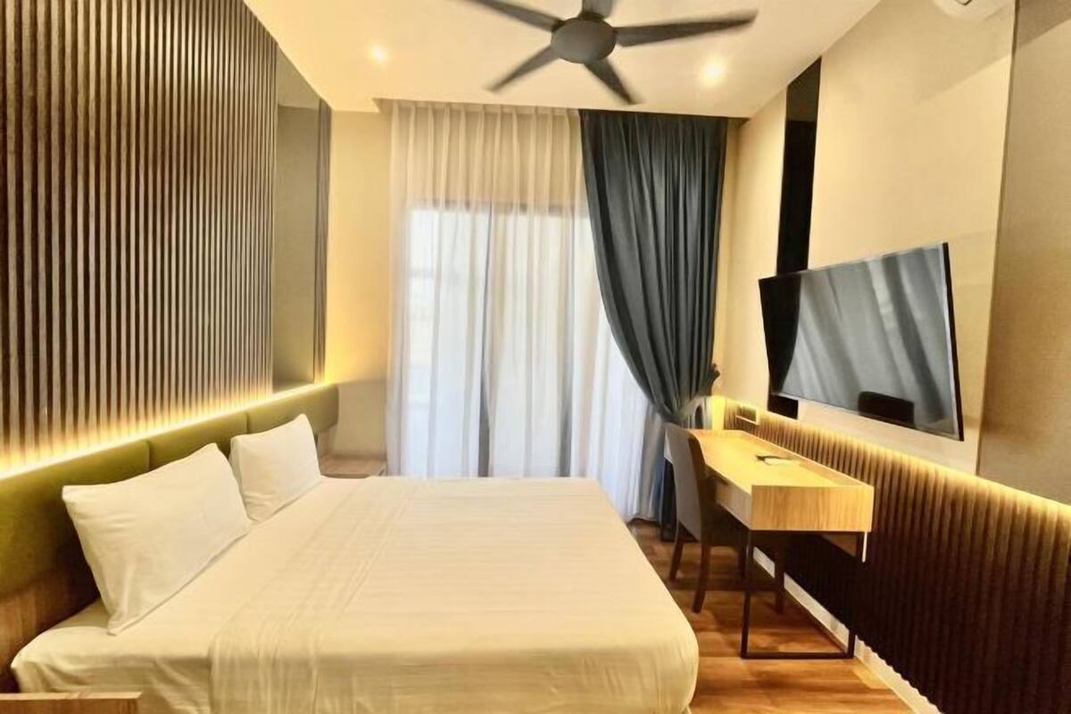 A modern hotel room with a bed, a desk, a flat-screen TV, a ceiling fan, and a window with curtains.