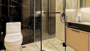 A modern bathroom with a glass shower enclosure, a toilet, and a sink with toiletries. - I-Vista Hotel (Tawau)