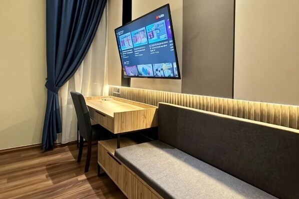 Quarto moderno com escrivaninha de madeira, um banco acolchoado, televisão de tela plana na parede e uma janela com cortinas.