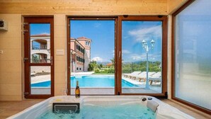 Een jacuzzi met een fles champagne, uitzicht op een zwembad en terras, en een gebouw met balkons op de achtergrond.