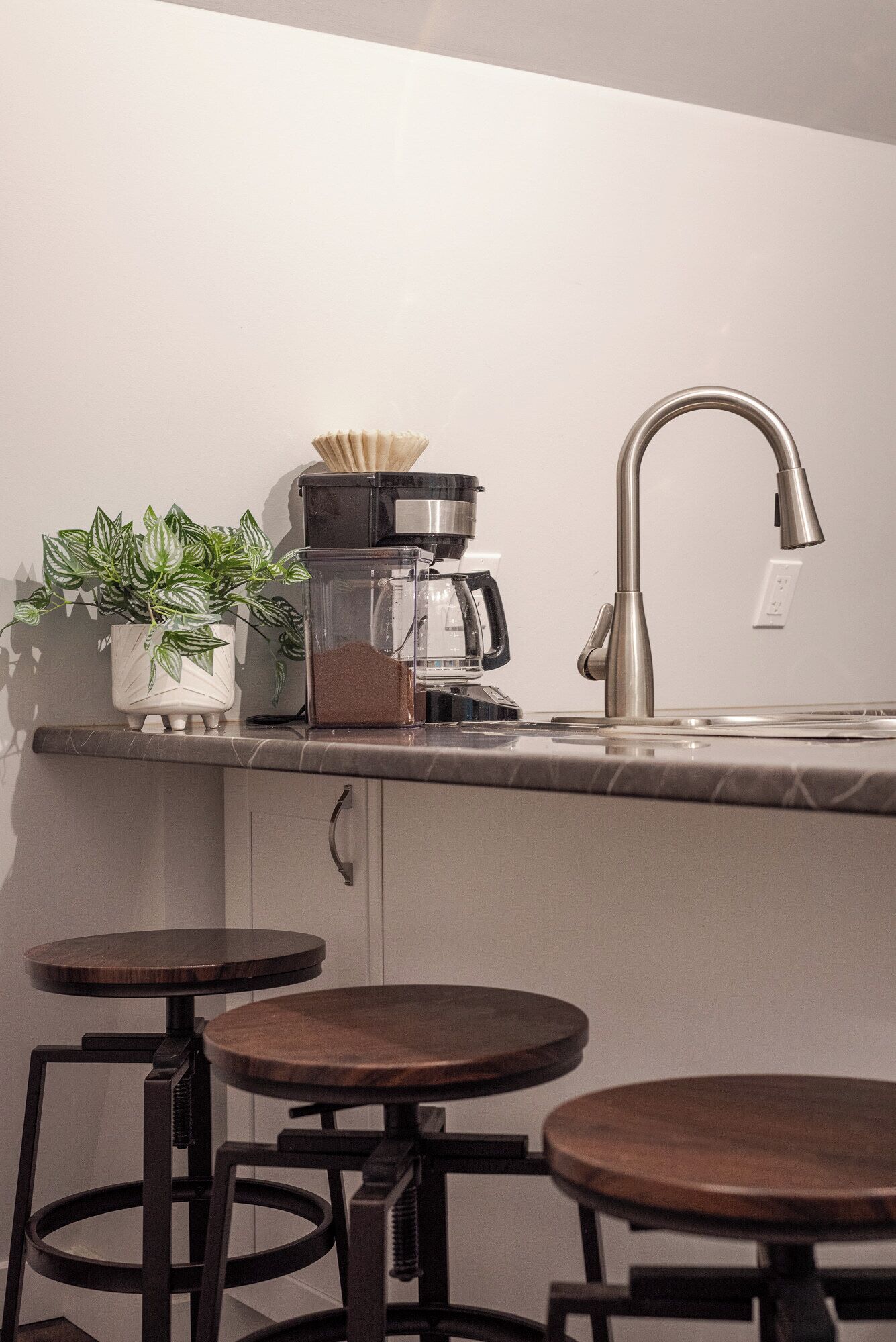 A kitchen with a coffee maker, a sink, and stools.