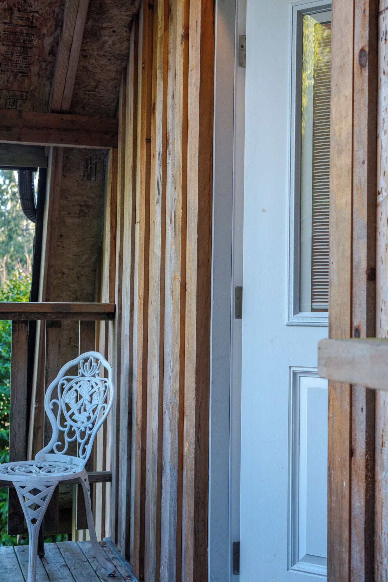 A wooden porch with a white metal chair and a door with a window.