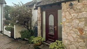 Une maison en pierre avec une porte en bois sombre, un petit porche et un chemin d’accès pavé de briques.