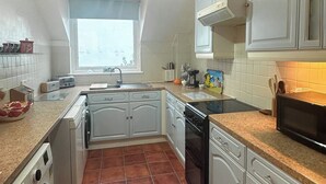 Une cuisine avec des meubles blancs, un évier, une cuisinière et un four à micro-ondes.