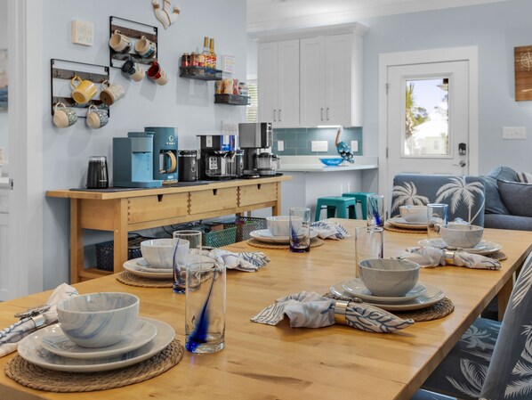 Una cocina moderna con una mesa de madera preparada para comer, una estación de café y vistas al área de estar.