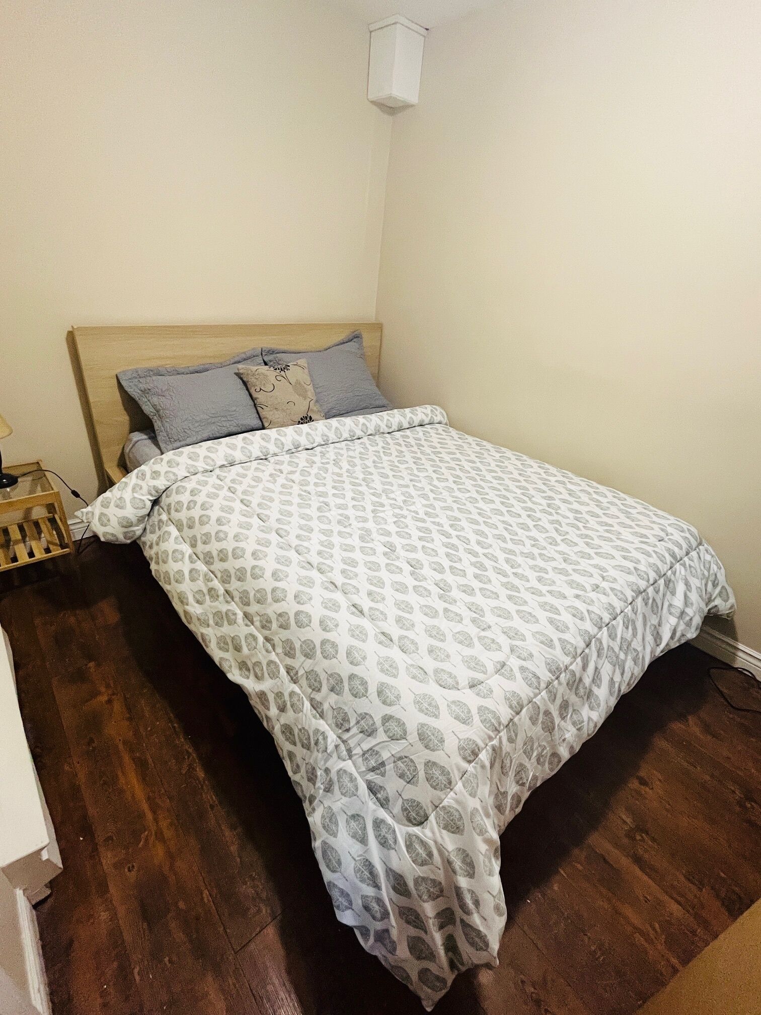 Een slaapkamer met een houten hoofdbord, een bed met een dessin en een nachtkastje met een lamp.