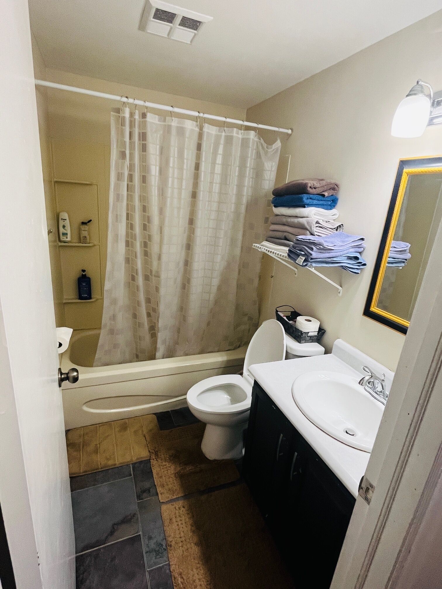 Une salle de bain avec une baignoire, des toilettes et un lavabo. Des serviettes et des articles de toilette sont disposés sur des étagères.