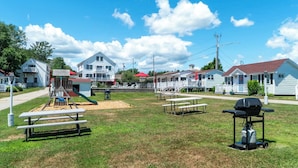Un espace verdoyant aménagé avec des tables de pique-nique, une aire de jeux et un barbecue, situé dans un quartier résidentiel.