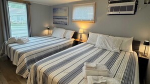 Une chambre d’hôtel avec deux lits, chacun doté de draps et d’oreillers à rayures, d’un ventilateur de plafond et d’un appareil de climatisation.