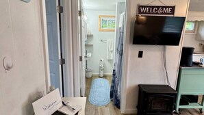 Un couloir avec une pancarte « Bienvenue », un mot d’accueil, une autre pancarte indiquant « Serendipity », une brochure intitulée « Bienvenue chez Serendipity », un téléviseur, une petite table avec une machine à café et un plancher en bois.