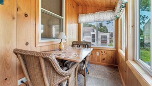 Una habitación con paneles de madera, una mesa de comedor, sillas de mimbre y una ventana con persianas.